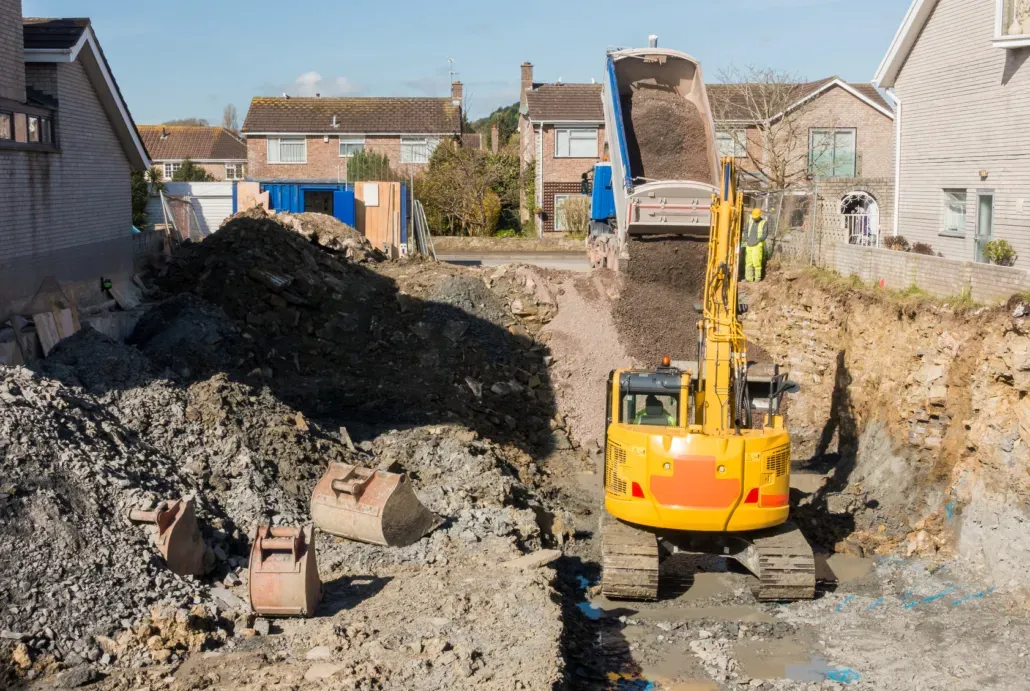 Heavy machinery conducting groundwork excavation and material delivery on a site.