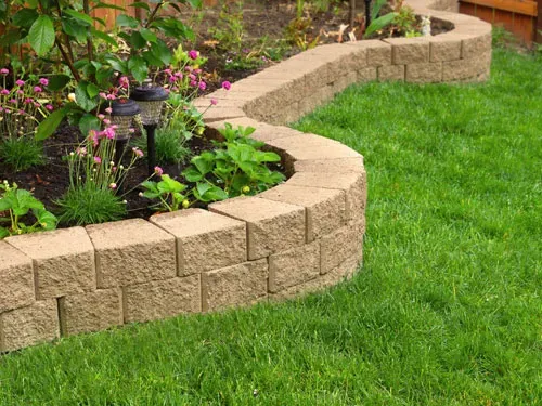Decorative curved garden wall made of paving blocks bordering a lawn and planting area.