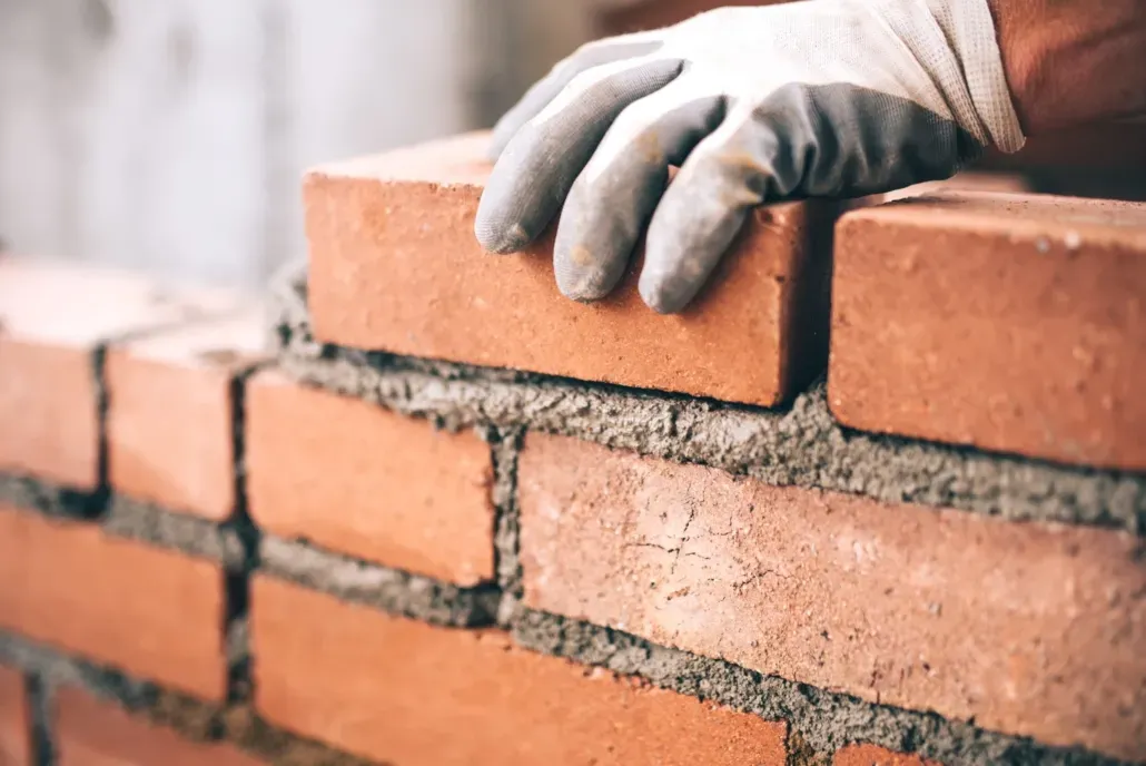 Close up of a hand laying a brick with mortar