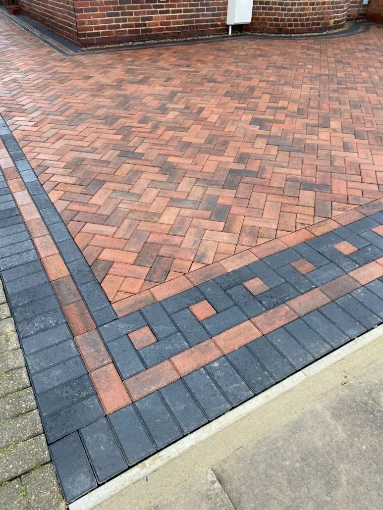 Detailed view of a newly laid block paving driveway in a herringbone pattern with red and brown blocks, bordered by black block paving.