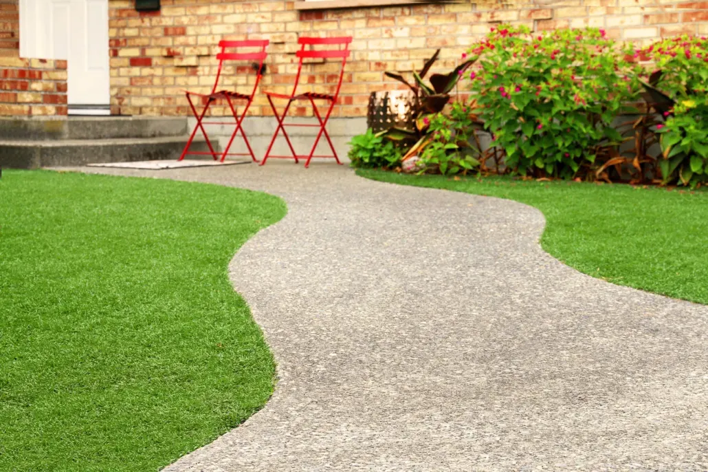 A winding garden pathway beside artificial grass leading towards a house.