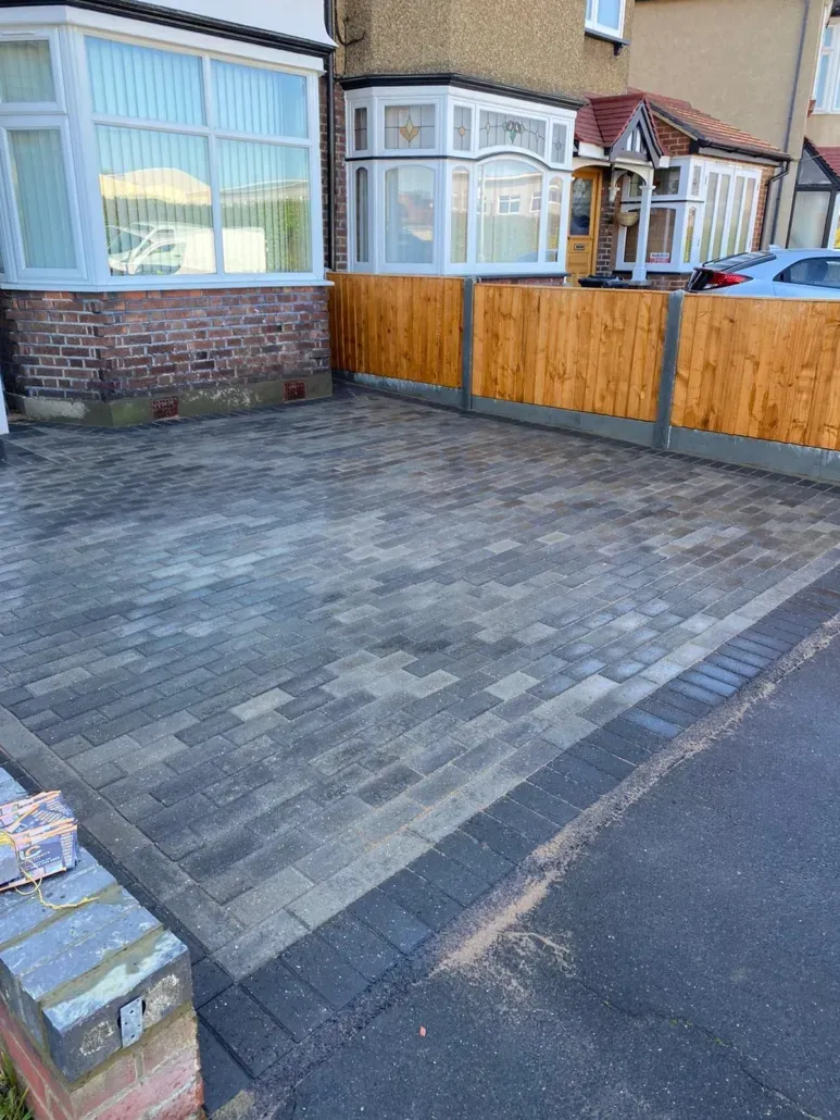 Newly laid grey block paving driveway with a darker border in front of a house.