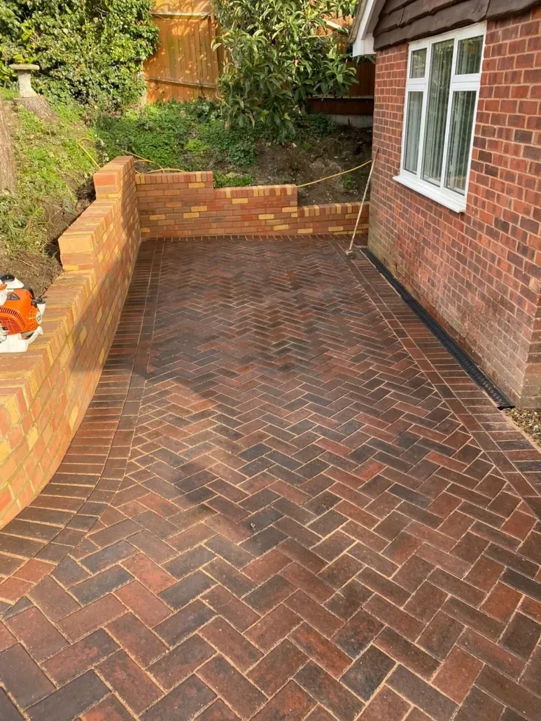 Newly laid block paving driveway in a herringbone pattern with a brick retaining wall.